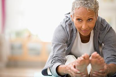 Older woman with gray hair smiling as she reaches toward her feet while stretching